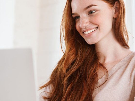 Junge Frau blickt lächelnd auf Laptop