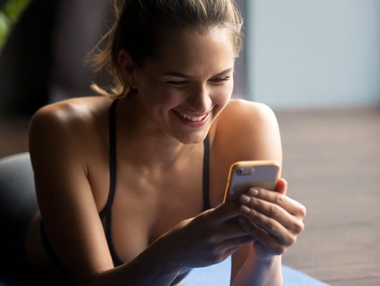 Frau auf Yogamatte blickt lächelnd auf Smartphone