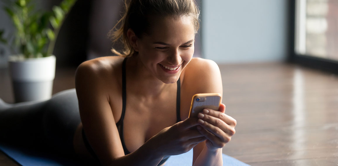 Frau auf Yogamatte blickt lächelnd auf Smartphone