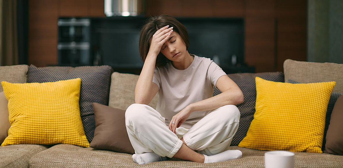 Frau auf Sofa leidet unter Kopfschmerzen