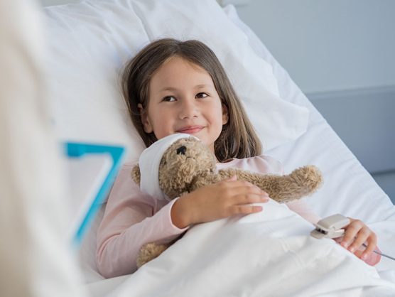 Lächelndes Mädchen mit Teddybär in Krankenbett