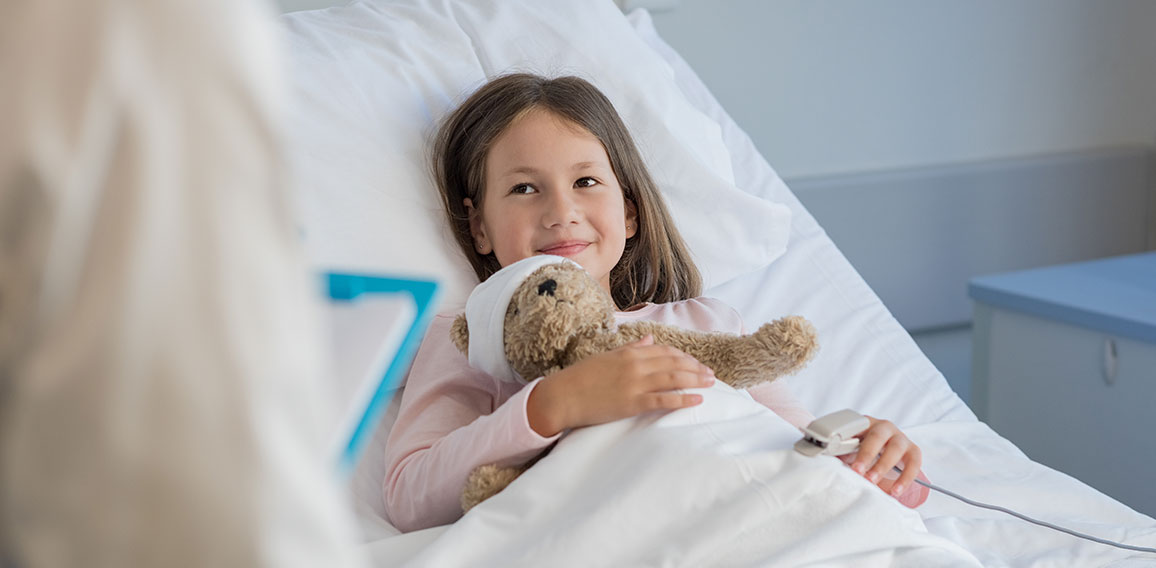 Lächelndes Mädchen mit Teddybär in Krankenbett