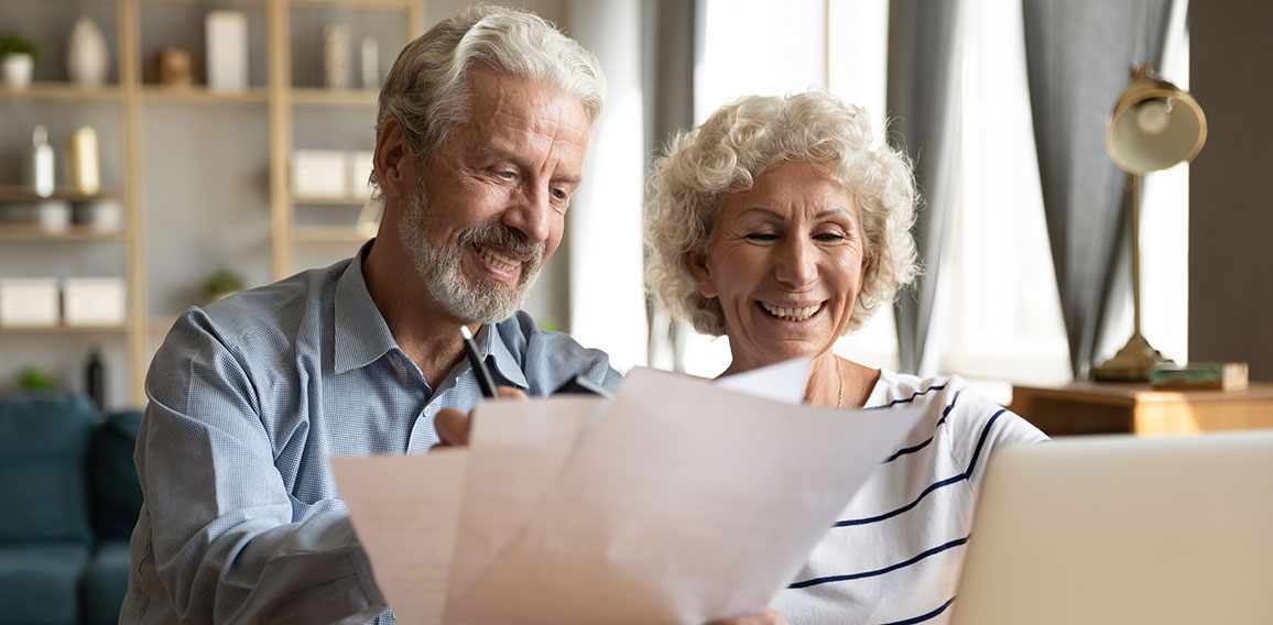 Senioren-Paar freut sich über Dokumente und Laptop