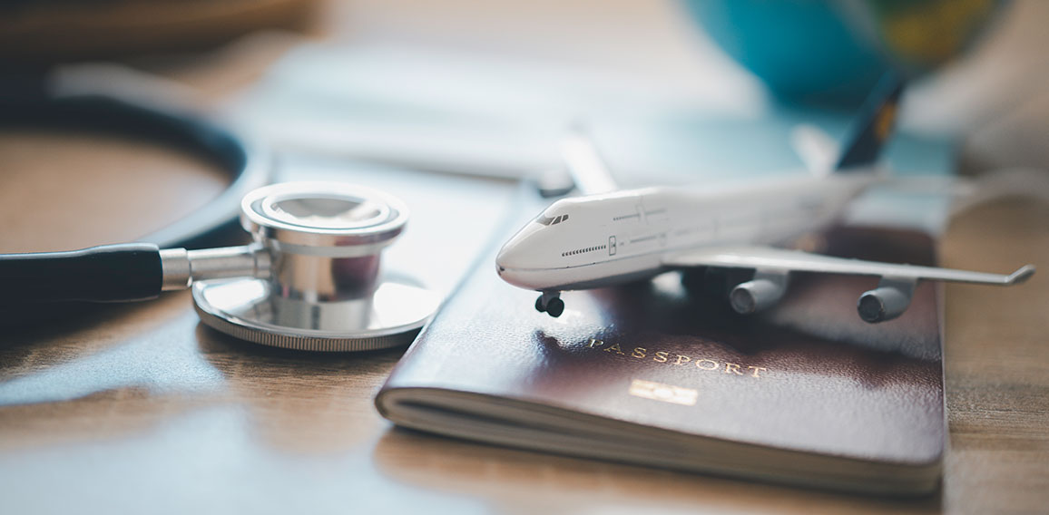 Stethoskop neben Reisepass und Miniaturflugzeug