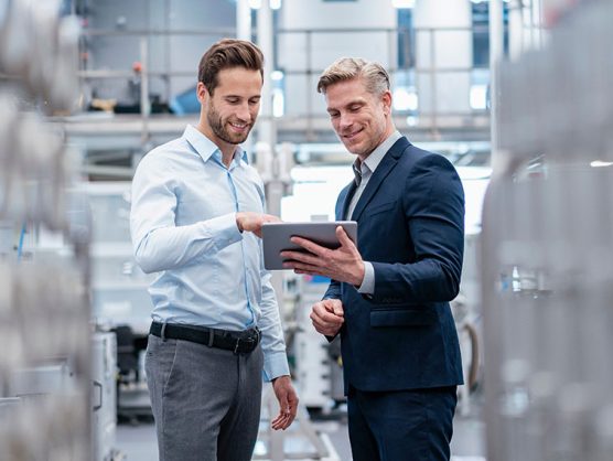 Anzugträger mit Tablet und Kunde in Fabrikhalle