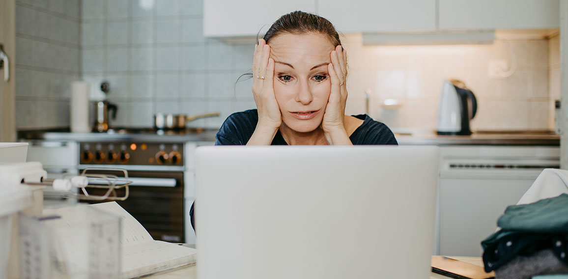 Geschockte Frau sitzt in Küche vor Laptop