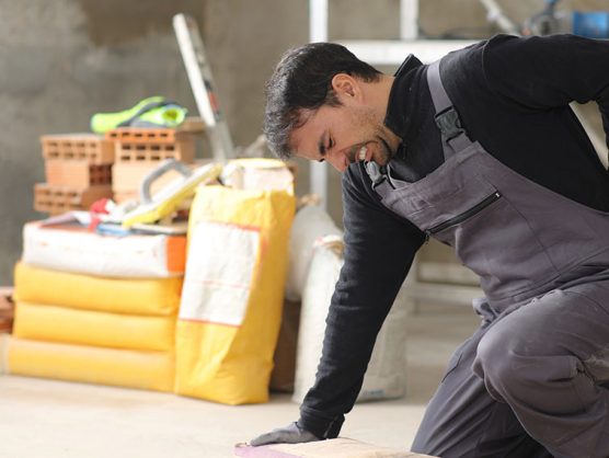 Handwerker auf Baustelle mit Rückenschmerzen