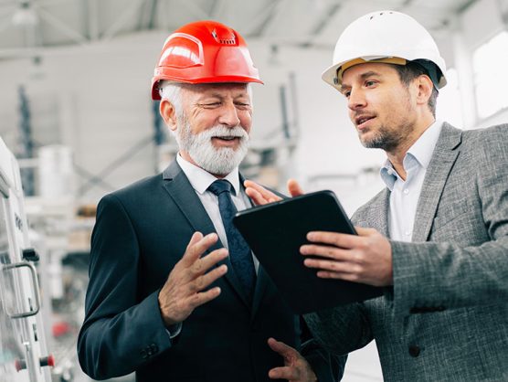 Zwei Anzugträger mit Tablet und Bauhelm in Fabrikhalle