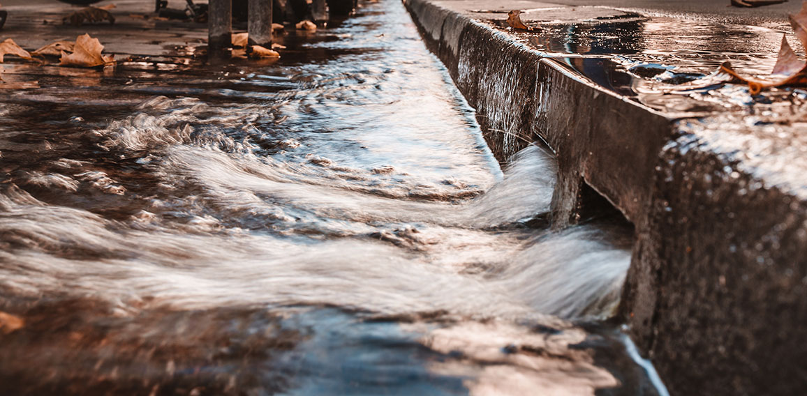 Stormy water on the sidewalk in a strong stream through curbs