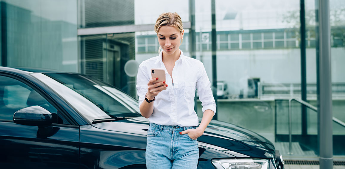 Female driver using smartphone near vehicle