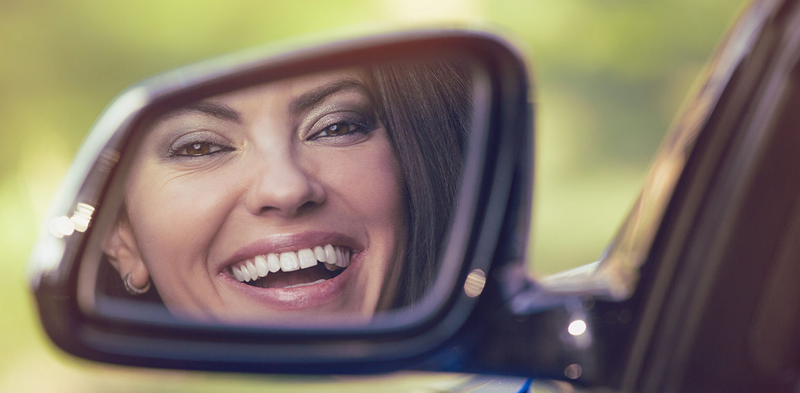 Happy woman driver looking in car side view mirror laughing