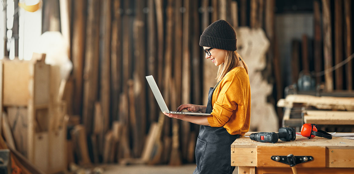 young female carpenter looks drawings on a laptop during a break in work in  workshop