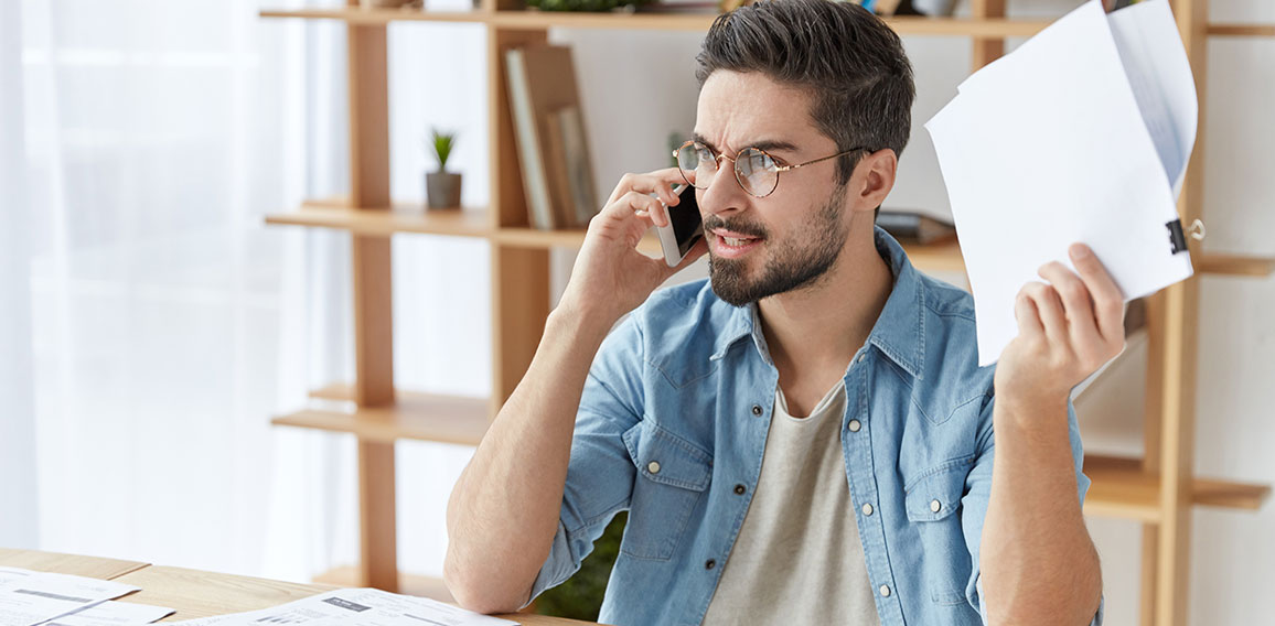 Shot of serious angry male enterpreneur tries to prove his rightness, has qaurrel with boss over smart phone, holds papers, solve company`s problems together. Annoyed boss shouts at colleague