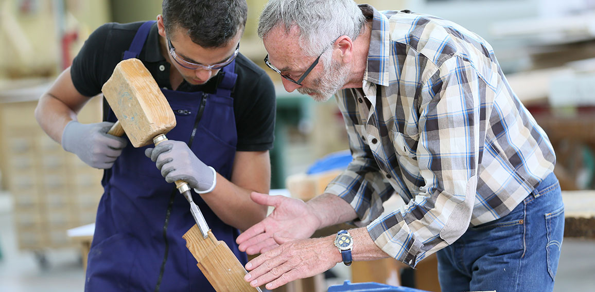 Young apprentice with teacher working on piece of wood