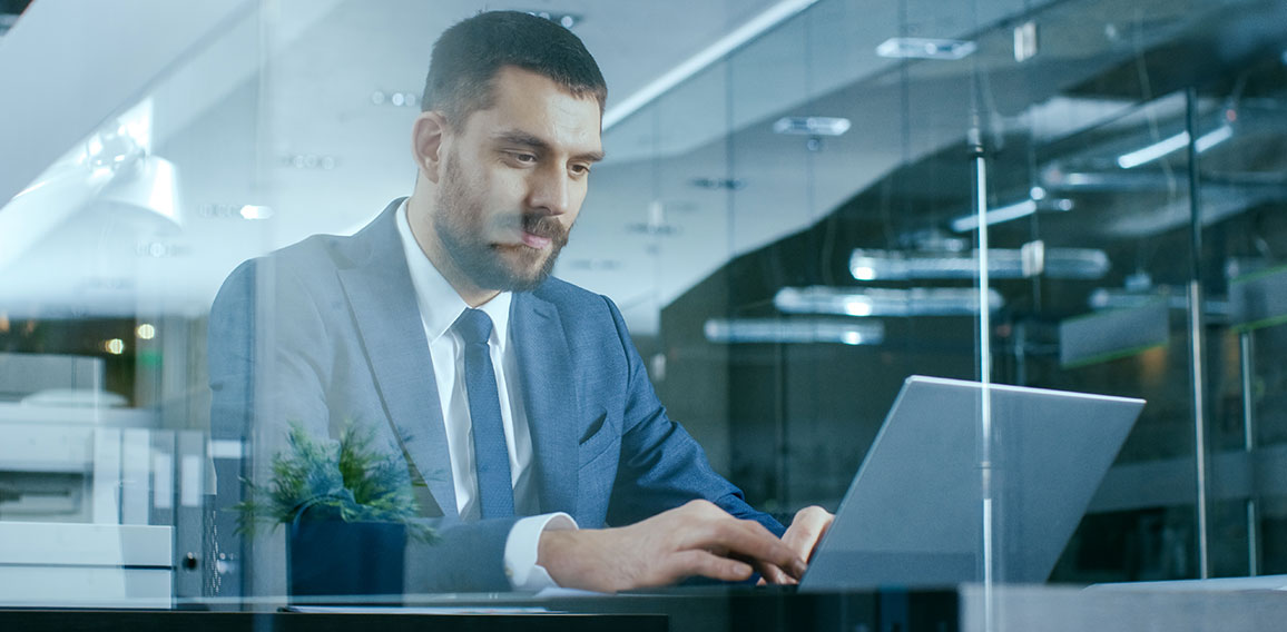 Confident Handsome Businessman Works on a Laptop at His Desk. St