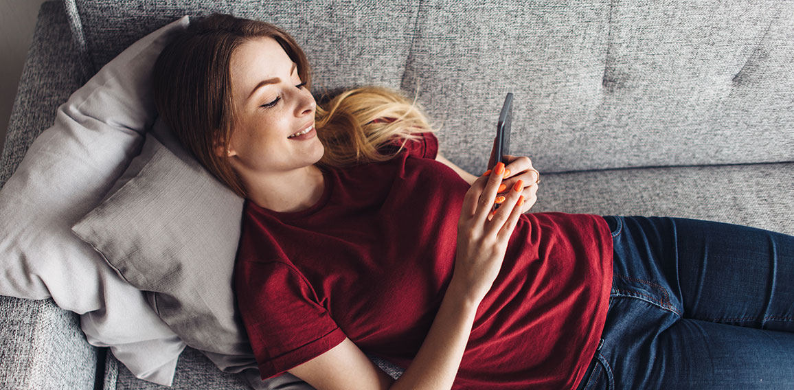 Girl using phone while lying on sofa at home