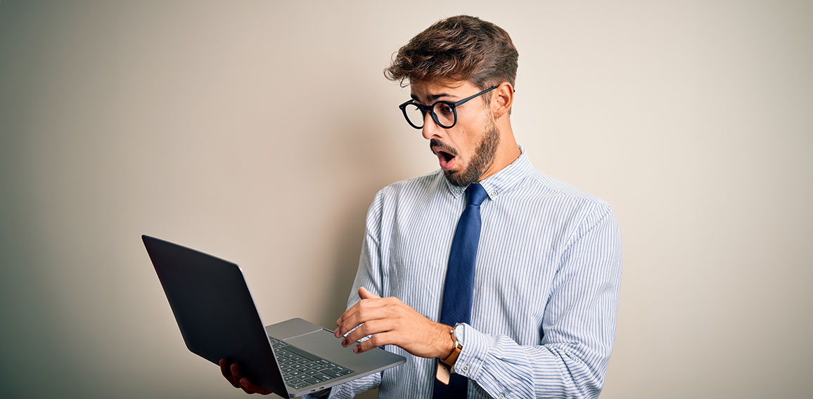 Young businessman wearing glasses working using laptop standing over white background scared in shock with a surprise face, afraid and excited with fear expression