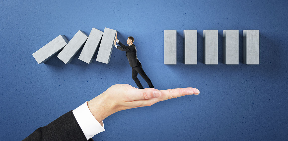 Business man hand holding abstract falling wooden blocks on blue wall background. Financial, crisis and challenge concept.