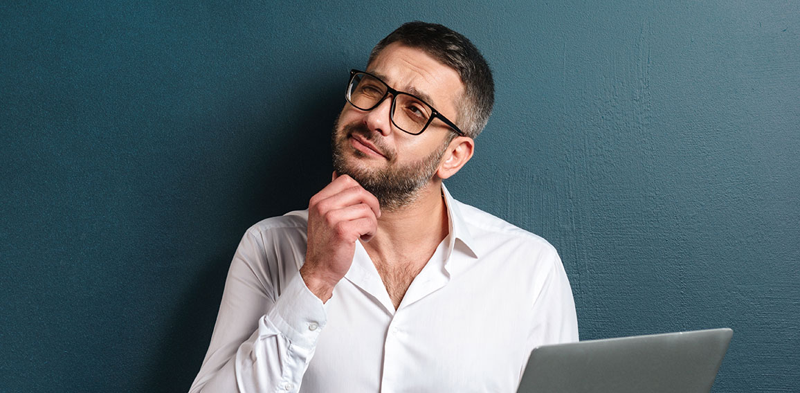 Thoughtful man wearing glasses using laptop computer.