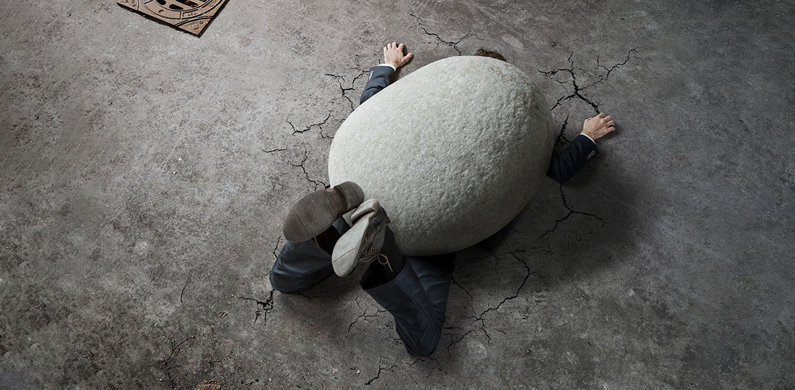 High angle view of businessman crushed by the huge stone on the