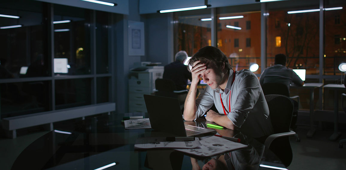 Portrait of exhausted stressed businessman work on laptop at night in dark office