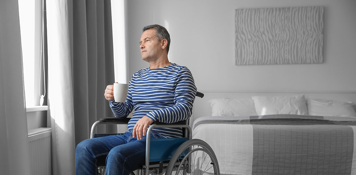 Mature man in wheelchair drinking coffee near window indoors