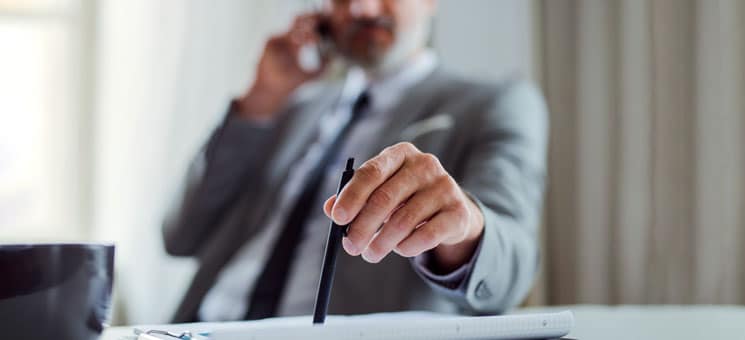 A midsection of businessman with smartphone sitting at the table, making a phone call.