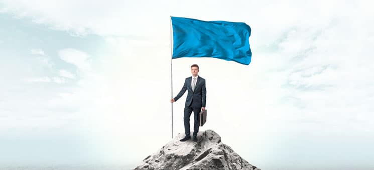 Businessman on the top of a the mountain holding flag