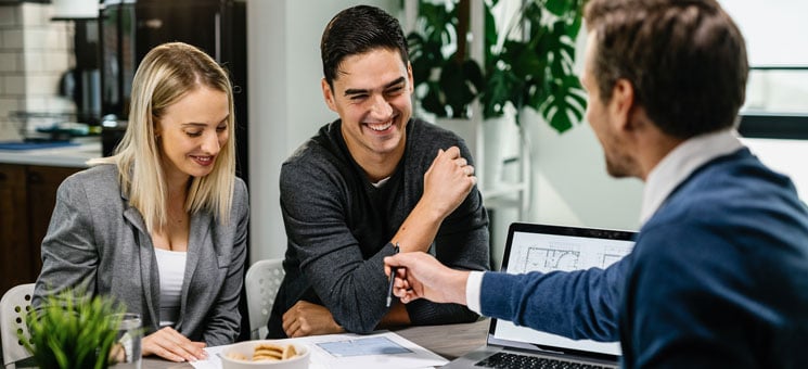 Young happy couple going through housing plans with real estate agent.