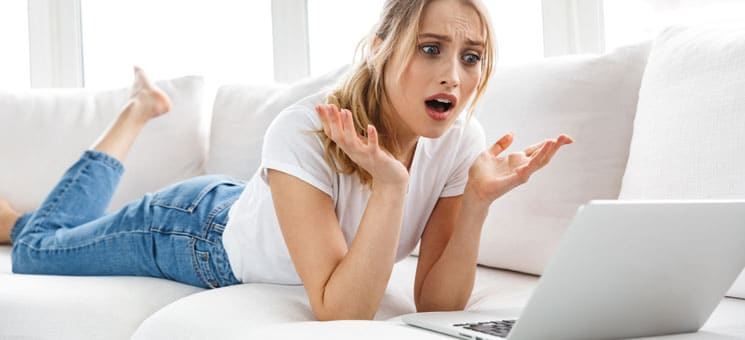 Portrait of outraged girl 20s using laptop while lying on couch