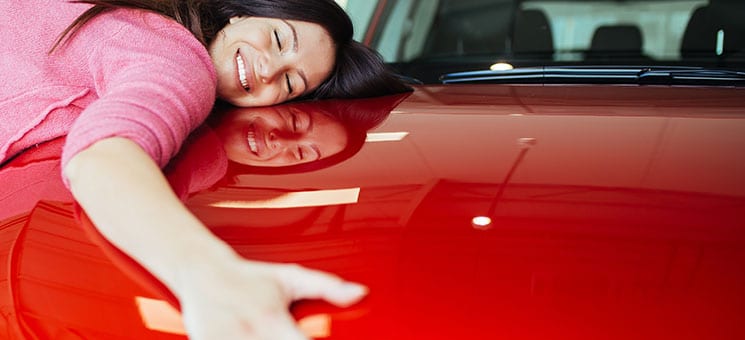 Happy beautiful young woman buying a new car at the car showroom