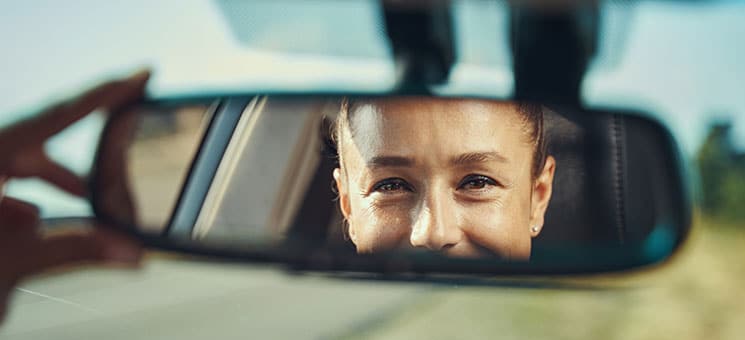 Happy woman looking at her face in rear-view mirror