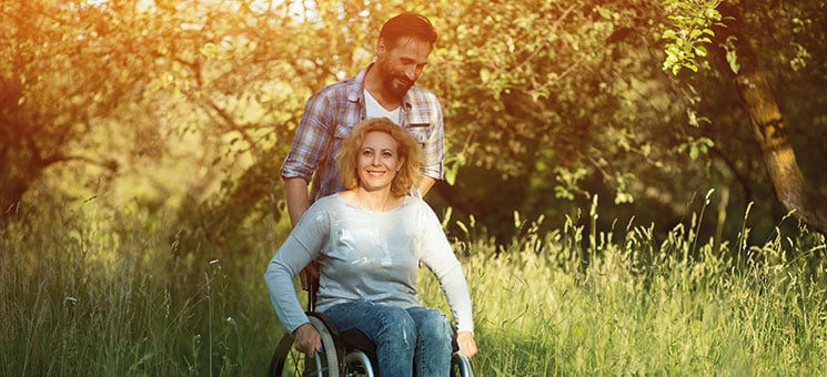 Smiling woman in wheelchair with husband in the park on sunny day