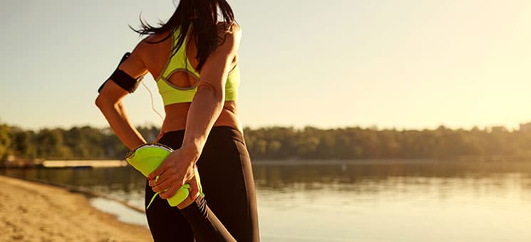 Young woman runner doing warm-up stretching her legs in a park.