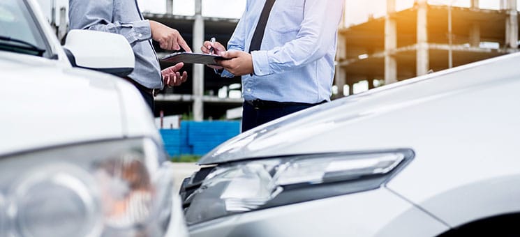 Insurance agent writing on clipboard while examining car after a