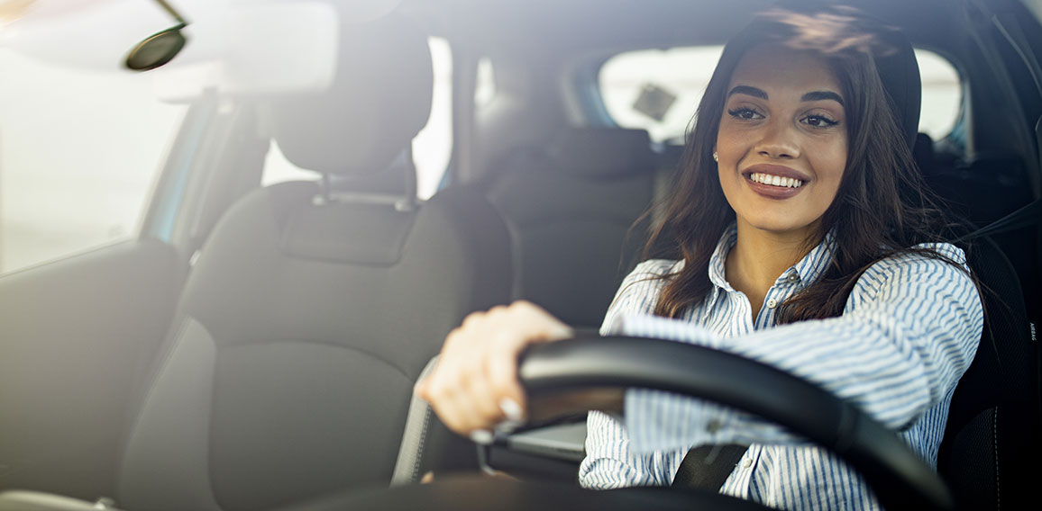 Beautiful young happy smiling woman driving her new car at sunse