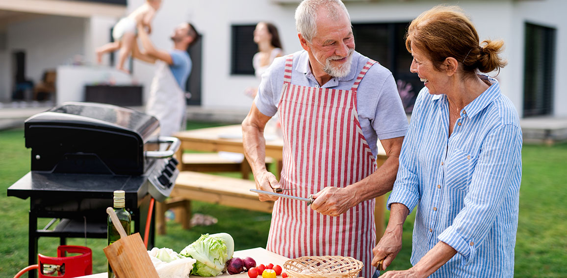 Senior couple with family outdoors on garden barbecue, grilling.