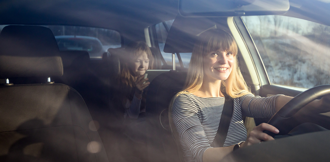 Mom driving car while her daughter sitting on back seat and usin