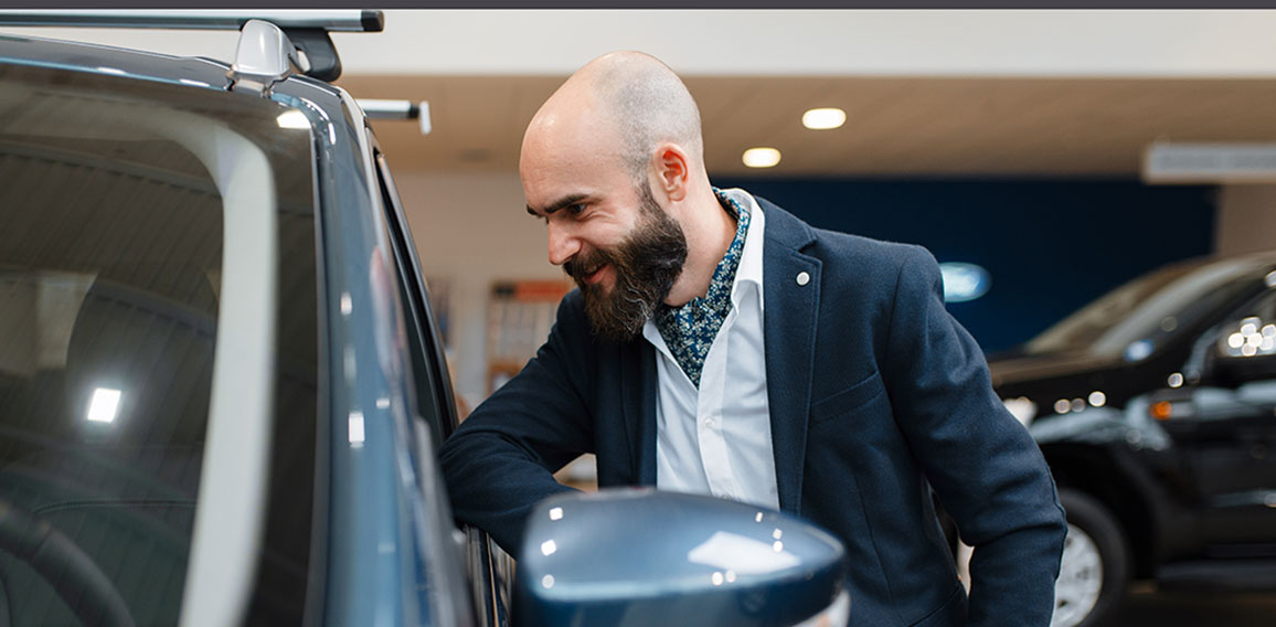 Smiling man poses at automobile in car dealership