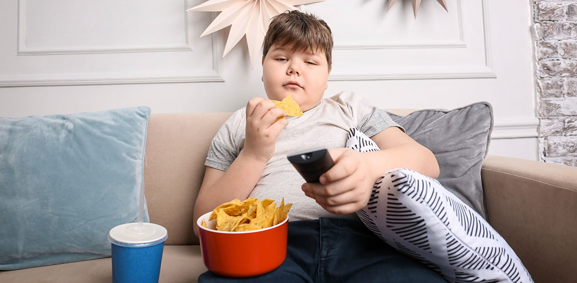 Overweight boy watching TV with snacks indoors