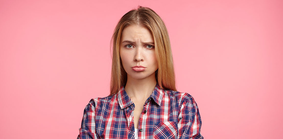 Portrait of offened unhappy beautiful woman keeps hands crossed, curves lips, displeased with everything, being abused by bad words and remarks from best friend, feels frustrated and very upset