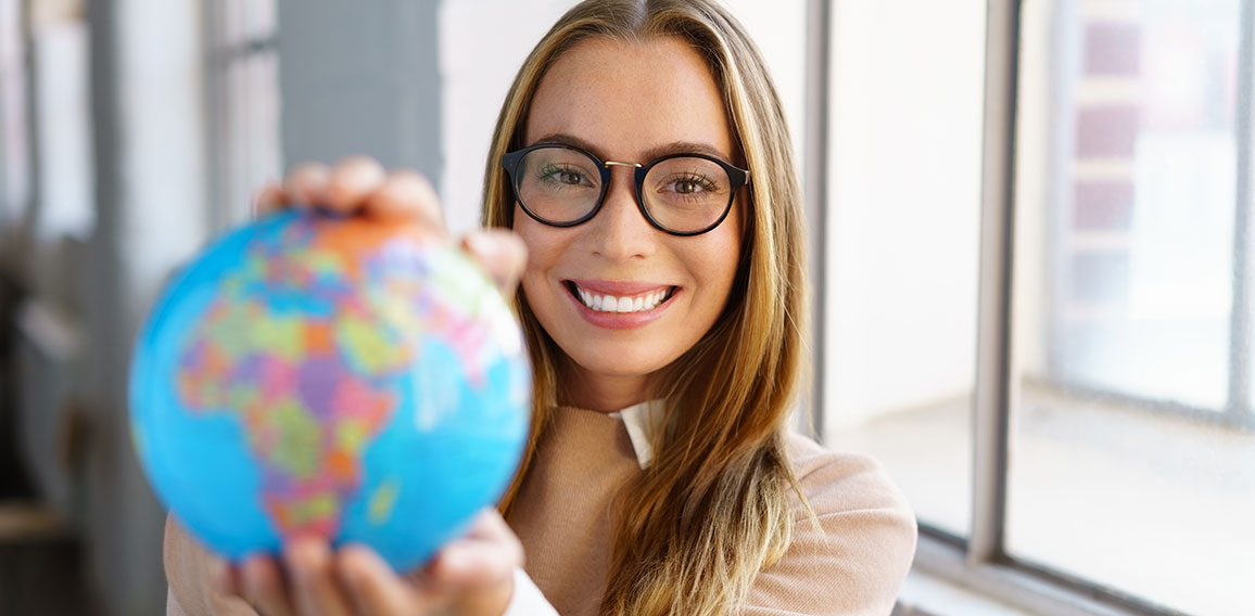 selbstbewusste junge frau mit brille hält einen globus in den händen