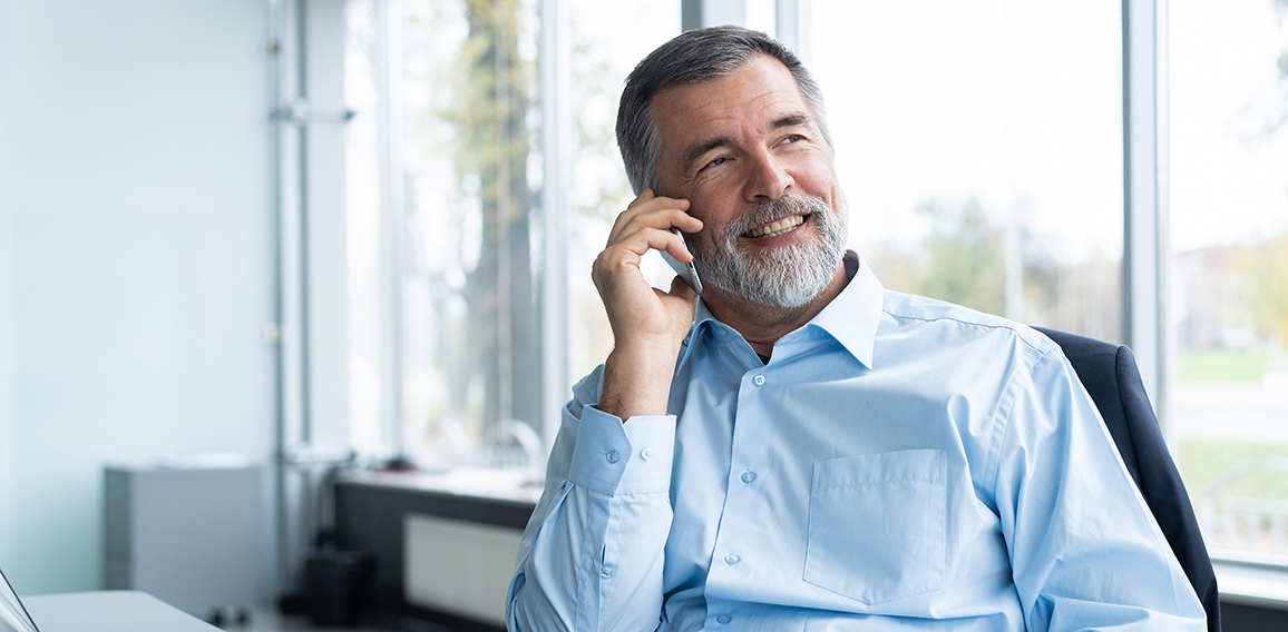 Executive senior businessman using his mobile phone and talking wih somebody while working laptop in the office.