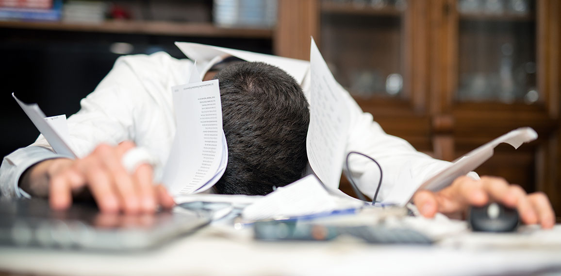 Desperate man submerged from work in his office. Papers and lapt