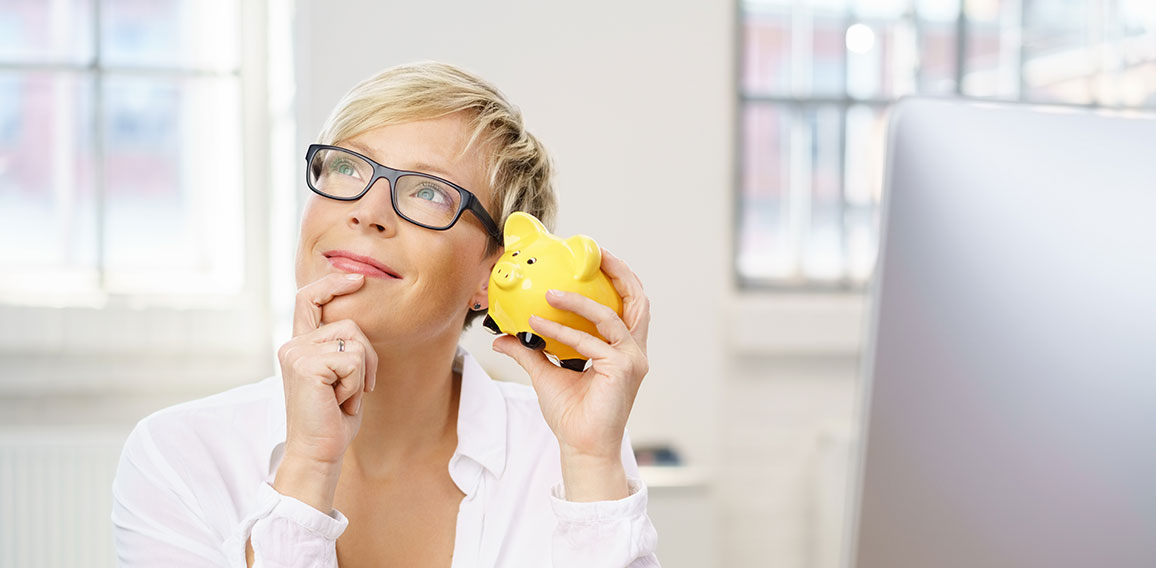 frau im büro hält nachdenklich ein sparschwein in der hand