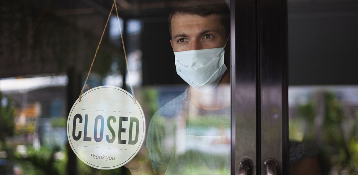 Chef in safety mask hanging up sign closed on restaurant door.