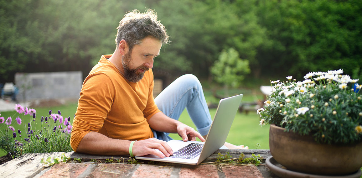 Mature man with laptop working outdoors in garden, home office concept.