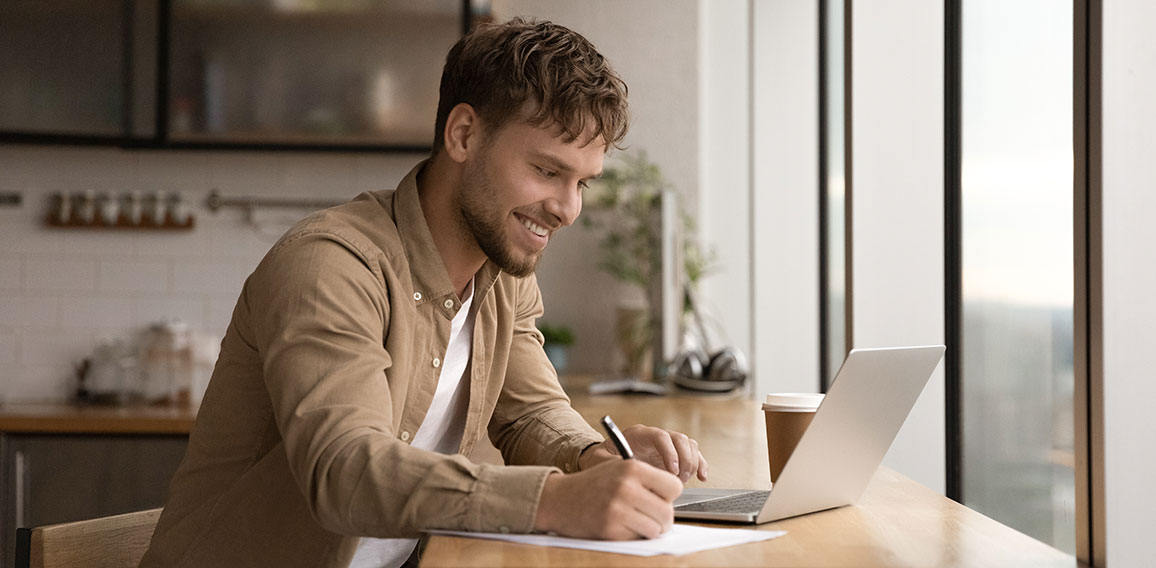 Close up smiling man using laptop, taking notes, studying online