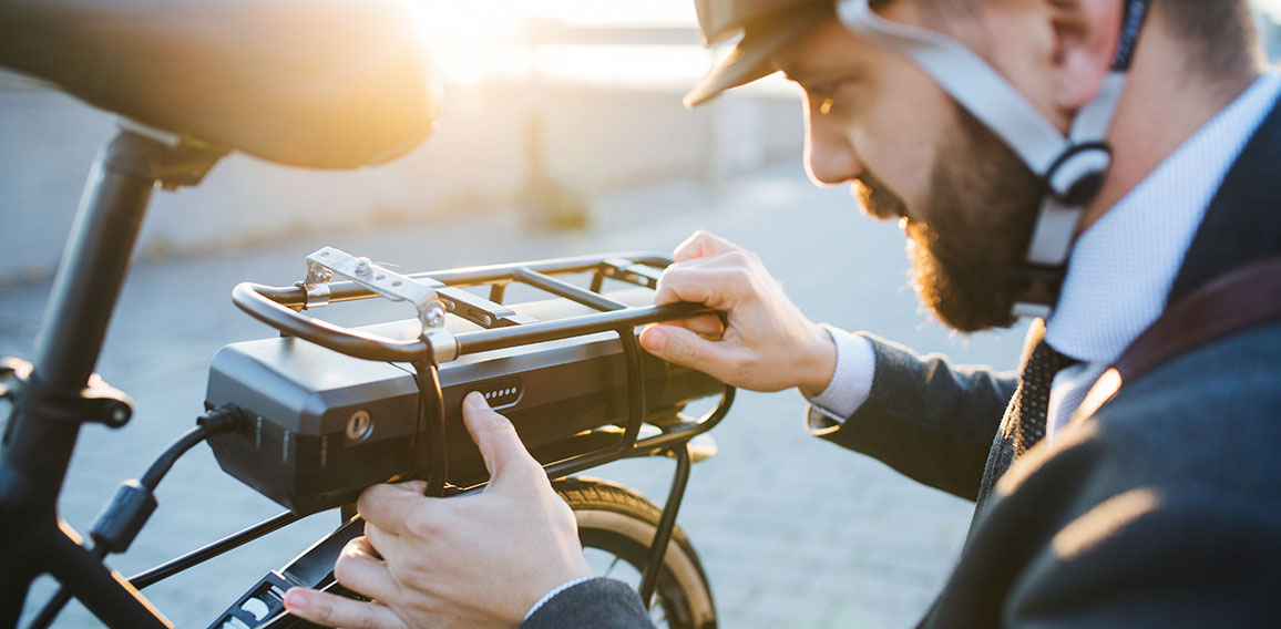 Hipster businessman commuter setting up electric bicycle in city.