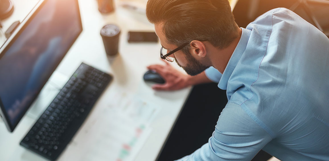 Work hard. Young bearded businessman in eyeglasses and formal wear using computer while standing in the modern office